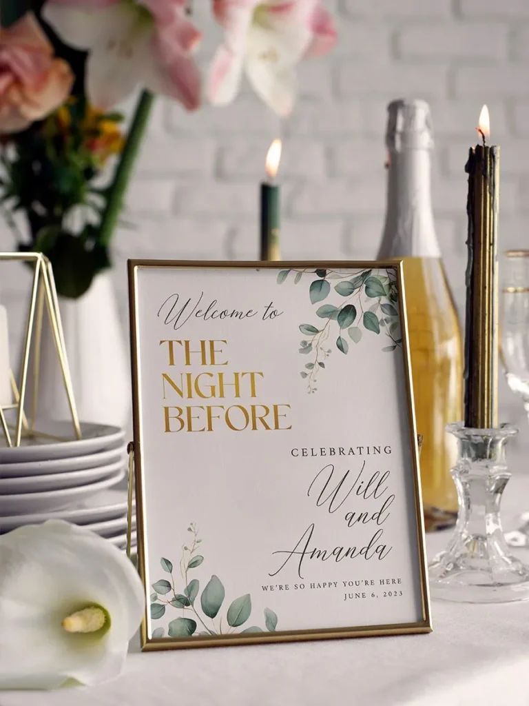 Personalized rehearsal dinner decor in thin gold frame with two names and custom date, displayed on table with dishes, bottle, flowers, and candles.