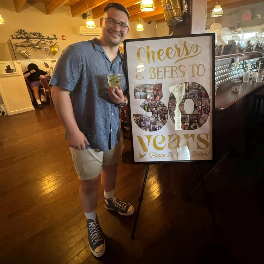 Smiling young man posing next to custom birthday photo collage made for him.